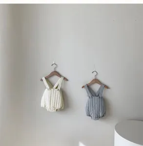 Detailed shot of baby quilted strap rompers in cream and grey hanging on hangers, thick and warm.
