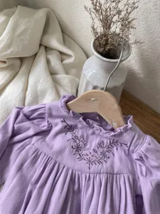 Detailed view of baby girl purple long-sleeve romper with floral embroidery and bud collar.