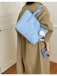 Vista detallada del elegante bolso tote azul claro con bordado colorido y colgante de peluche.