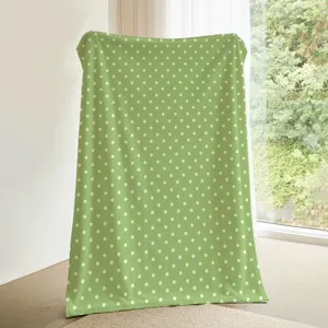 Detalle de manta de franela con lunares verdes que muestra textura suave y calidez acogedora.