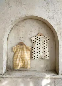 Detail view of cute baby rompers hanging on wooden hangers against a textured wall.