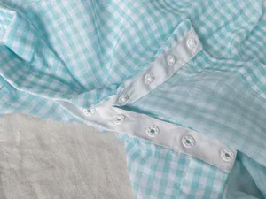Close-up detail of light blue and white gingham baby apparel fabric with snap buttons.
