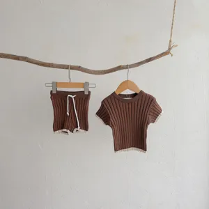 Détail ensemble pull bébé, top manches courtes et short marron doux avec bordure contrastée.