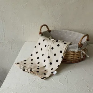 Detailed shot of beige sleeveless baby romper with black polka dots and front button closure.