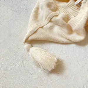 Vista detallada de un jersey de punto crema para bebé con borla y textura suave.