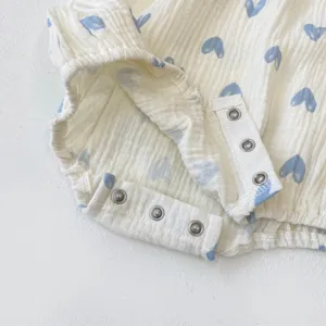 Detail shot of infant cotton gauze romper showcasing snap buttons and blue heart print pattern.