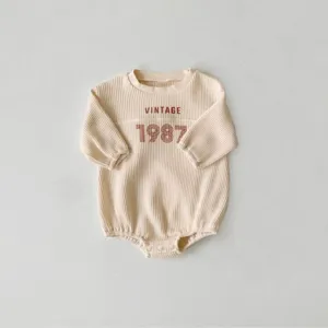 Close-up detail of infant baby waffle knit romper with vintage 1987 chest print design.