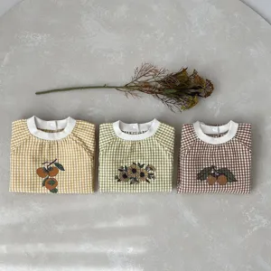 Closeup of cute baby cotton rompers with plaid patterns and lovely botanical embroidery details.