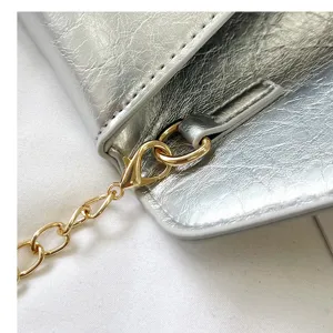 Detail shot of stylish silver envelope shoulder bag with gold chain hardware and metallic texture.