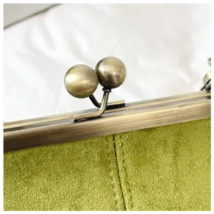 Close-up detail of vintage metal kiss lock clasp and green suede fabric women bag accessory.