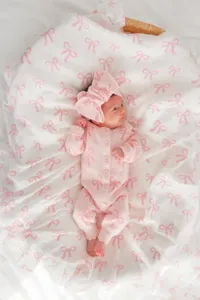Pink knitted baby romper with cute bow pattern and matching headband for infant girls.