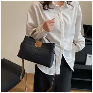 Close-up of black crocodile pattern shoulder bag with brown straps worn by model indoors.