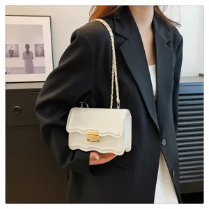 Detailed view of white chic shoulder bag featuring unique wavy flap and metal chain strap.