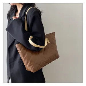 Detail view of a stylish brown quilted tote bag with contrast cream straps worn by model.