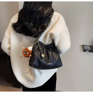 Detail view of a stylish black pleated shoulder bag with chain strap and cute plush charm.