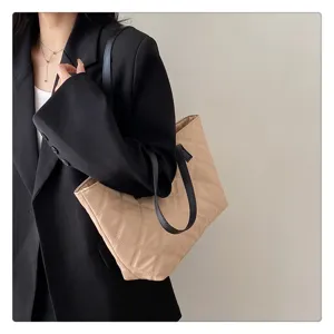 Detailed shot of a stylish beige quilted tote bag with black straps, showcasing soft texture.