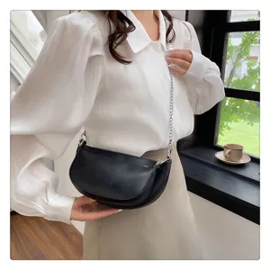 Black leather crescent saddle bag with metal chain strap worn by model, detail view.