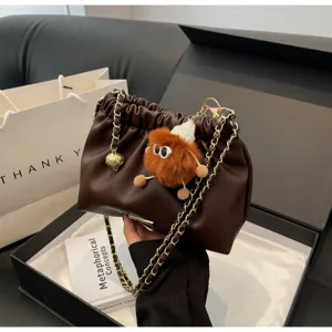 Detailed shot of dark brown gathered shoulder bag with gold chain and plush toy pendant.