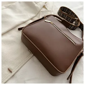 Brown leather crossbody bag for women with wide monogram strap and zip pocket detail.