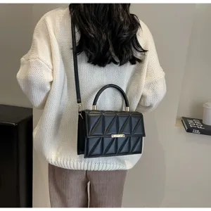 Detailed view of black quilted crossbody bag with chic metallic lock and top handle in setting.