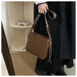 Brown leather crossbody bag with wide patterned strap and stylish tassel detail for daily commute.