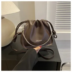 Dettaglio della borsa a secchiello marrone plissettata con catena metallica e coulisse.