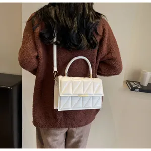 Close-up detail shot of a stylish white quilted crossbody bag worn with a brown sweater.