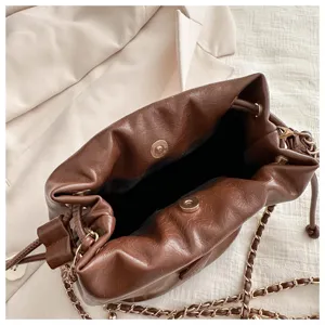 Detailed view of brown leather bucket bag with metallic chain strap and magnetic snap closure.