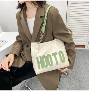 Detail shot of the large capacity canvas tote bag with green letter patch and chain strap.