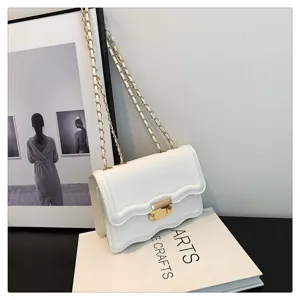 Detailed view of white wavy flap shoulder bag with gold chain strap displayed on art book.