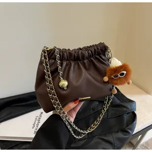 Detailed view of dark brown pleated leather shoulder bag with chain strap and fluffy charm.