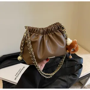 Detailed shot of trendy brown cloud shoulder bag with gold chain strap and plush charm.