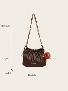 Detailed view of brown ruched shoulder bag with chain strap and cute furry monster pendant.
