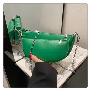 Green saddle shoulder bag detail, metal chain strap and dual zipper design close-up view.
