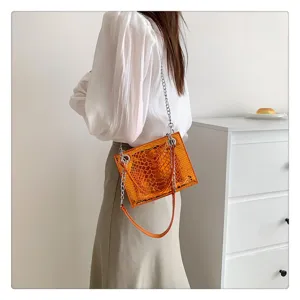 Gros plan détaillé du sac à main brillant effet croco avec chaîne porté par le mannequin.
