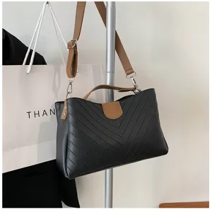 Detailed close-up view of a chic black shoulder bag featuring brown straps and chevron stitching.