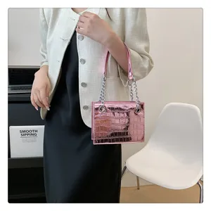 Detailed view of a stylish pink metallic crocodile pattern chain handbag worn by model in room.