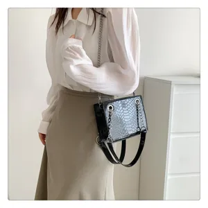 Gros plan détail du sac à épaule pour femme en cuir vernis motif crocodile noir.