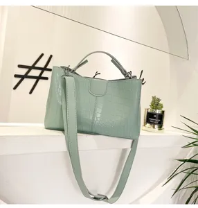 Light green crocodile pattern handbag with top handle and adjustable crossbody strap.