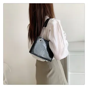 Vue détaillée d'un élégant sac bandoulière noir verni motif crocodile avec chaîne métallique.