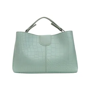 Close-up detail of the mint green crocodile textured handbag featuring neat stitching and handles.
