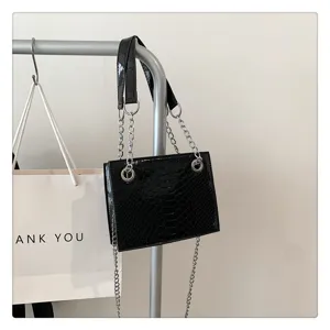 Gros plan détail du sac chaîne en cuir verni noir suspendu sur support métal pour la mode.
