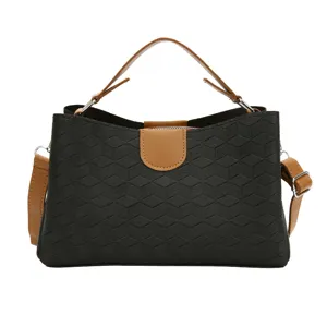 Detailed view of black geometric textured handbag with brown top handle and adjustable strap.