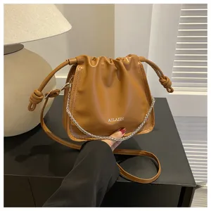 Dettaglio borsa a secchiello plissettata in pelle PU marrone, con catena trendy e tracolla regolabile.