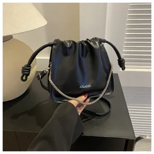 Vista dettagliata della borsa a secchiello nera con pieghe chic e catena elegante.