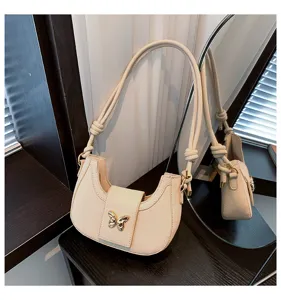 Trendy minimalist beige shoulder bag with chic gold butterfly metal accent and stylish strap knots.