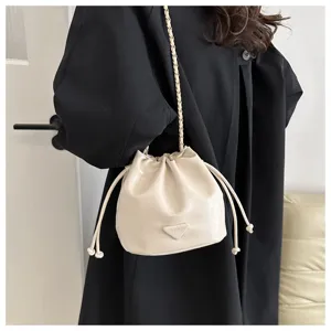 Detail view of trendy beige bucket bag featuring a chic chain strap and drawstring.