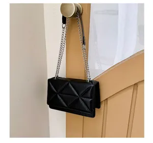 Nahaufnahme der schwarzen gesteppten Umhängetasche mit geometrischer Klappe und Metallkette.