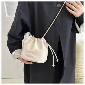 Beige leather bucket bag with metal chain strap, drawstring closure and chic triangular front badge.