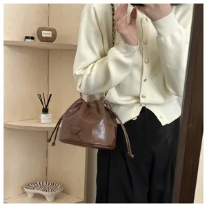Brown leather drawstring bucket bag with chain strap, stylish everyday shoulder and crossbody bag.